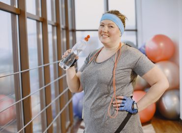 Adult fat woman doing gymnastics at the gym Fat woman dieting, fitness. Lady with rope. Woman in gray sportsuit.